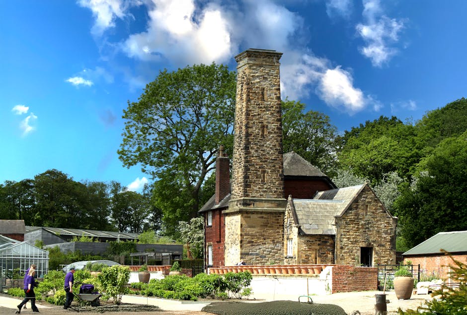 A tranquil river scene with lush green trees and tall grass lining the water's edge. A small brick structure with a domed roof, possibly a historic monument or garden feature, is partially obscured by